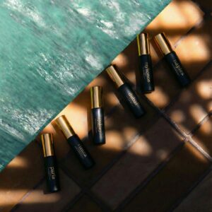 JoeJo+Nebria six mini luxury fragrance sprays styled beside turquoise water featuring Paris, Vienna, Sydney, Dubai, Mykonos and Naples