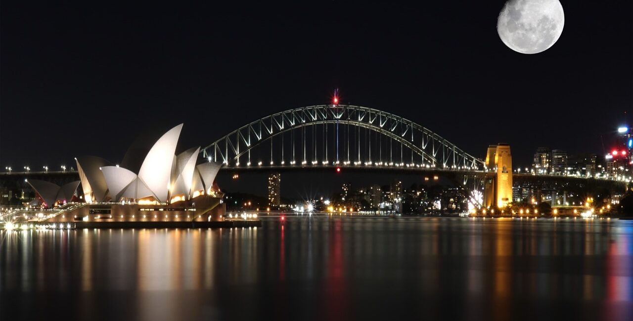 Sydney Opera House and Harbour Bridge at night with full moon over the harbor, illuminated skyline