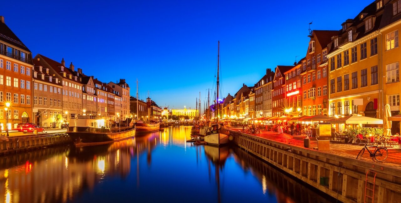Copenhagen Nyhavn waterfront at night with colorful buildings, reflections, and boats